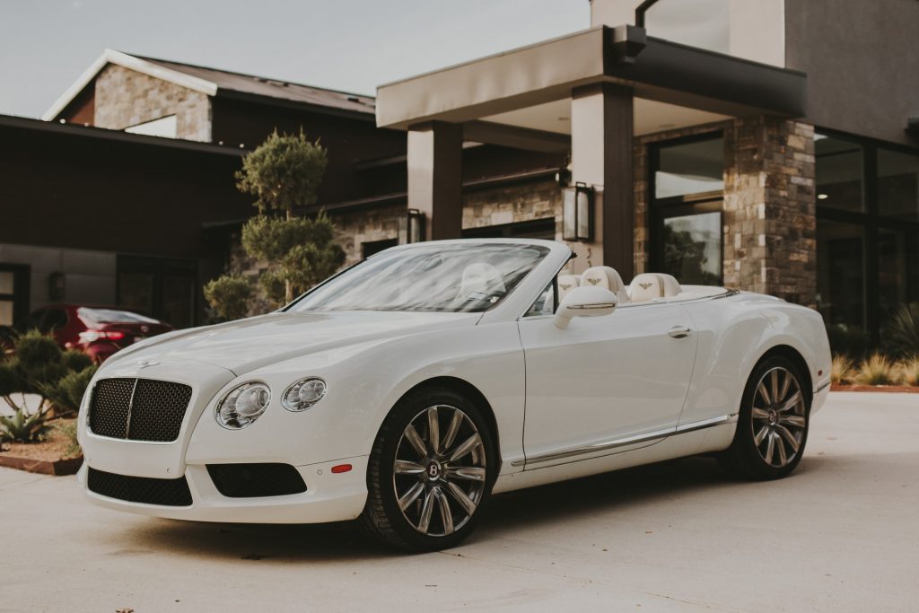 A pristine-looking white Bentley convertible outside of a modern mansion